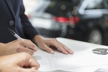 Close up customer signing financial contract paperwork in car dealership - CAIF20053