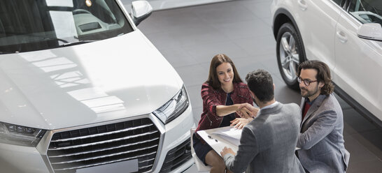 Car salesman shaking hands with female customer in car dealership showroom - CAIF20057