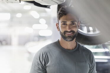 Porträt eines lächelnden, zuversichtlichen Mechanikers unter einem Auto - CAIF20059