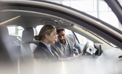 Car salesman showing new car to woman in driver’s seat at car dealership - CAIF20064