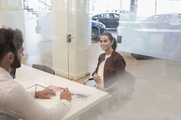 Autoverkäufer im Gespräch mit einer schwangeren Kundin im Büro eines Autohauses - CAIF20071