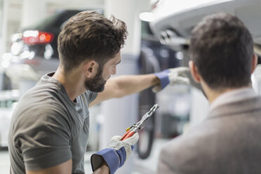 Auto mechanic with tool pointing, explaining to customer in auto repair shop - CAIF20074