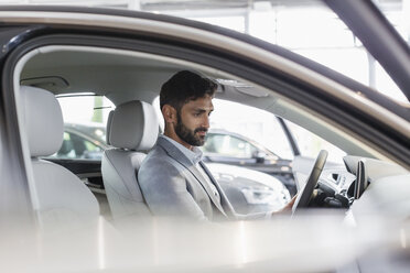 Male customer sitting in driver’s seat of new car in car dealership showroom - CAIF20076