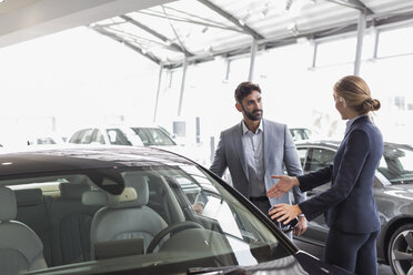 Car saleswoman showing new car to male customer in car dealership showroom - CAIF20079