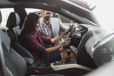 Car salesman and female customer in driver’s seat of new car in car dealership showroom - CAIF20080