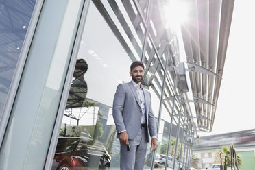 Portrait confident car salesman standing outside of car dealership showroom - CAIF20083