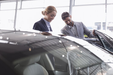 Autoverkäufer zeigt einer Kundin im Ausstellungsraum eines Autohauses ein neues Auto - CAIF20086