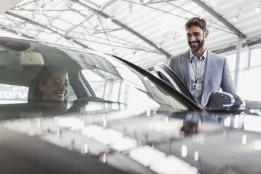 Smiling car salesman and female customer in driver’s seat of new car in car dealership showroom - CAIF20095