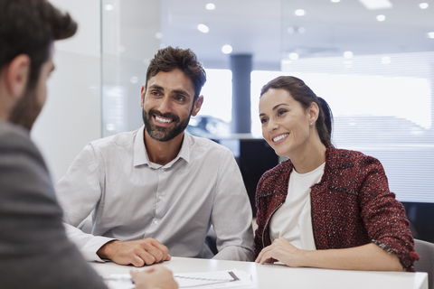 Lächelndes Kundenpaar im Gespräch mit einem Autoverkäufer im Büro eines Autohauses, lizenzfreies Stockfoto