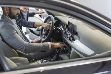 Autoverkäuferin zeigt und erklärt einem männlichen Kunden auf dem Fahrersitz ein neues Auto - CAIF20097