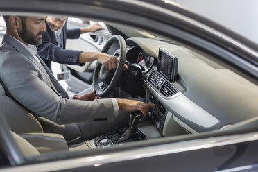 Car saleswoman pointing, explaining new car to male customer in driver’s seat - CAIF20097