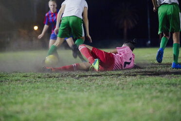 Junge Fußballspielerin, die den Ball beim Fußballspielen auf einem nächtlichen Feld kickt - CAIF20102