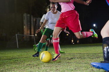 Junge Fußballspielerinnen spielen nachts auf einem Feld und treten den Ball - CAIF20104