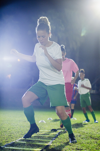 Junge Fußballspielerinnen üben nachts auf einem Spielfeld Beweglichkeitsübungen, lizenzfreies Stockfoto