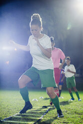 Junge Fußballspielerinnen üben nachts auf einem Spielfeld Beweglichkeitsübungen - CAIF20110