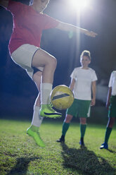 Junge Fußballspielerin beim Üben, Springen und Treten des Balls auf einem nächtlichen Feld - CAIF20112
