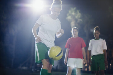 Fokussierte junge Fußballspielerin, die nachts auf dem Feld übt und den Ball mit dem Knie trifft - CAIF20115