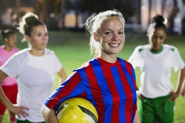 Portrait smiling, confident young female soccer player with ball on field at night - CAIF20116
