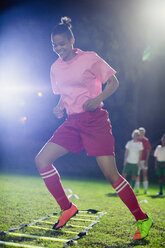 Junge Fußballspielerinnen üben nachts auf einem Spielfeld Beweglichkeitsübungen - CAIF20120
