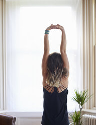 Frau übt Yoga, streckt die Arme über Kopf am Fenster - CAIF20130