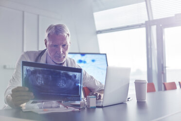 Fokussierter männlicher Chirurg, der Röntgenbilder am Laptop im Krankenhaus untersucht - CAIF20172