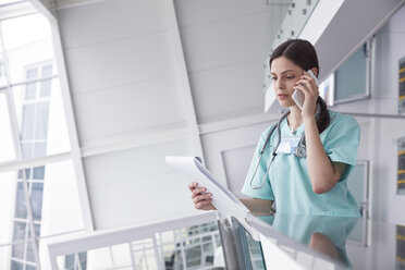 Weibliche Krankenschwester mit Klemmbrett, die in einem Krankenhaus mit einem Handy telefoniert - CAIF20183