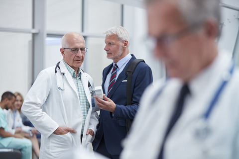 Männlicher Pharmareferent zeigt einem Arzt im Krankenhaus verschreibungspflichtige Medikamente, lizenzfreies Stockfoto