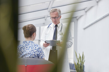 Männlicher Arzt mit Klemmbrett im Gespräch mit einer Patientin in der Krankenhauslobby - CAIF20192