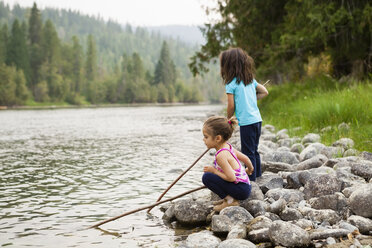 Girl sisters playing with sticks at lakeside - CAIF20204