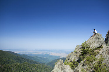 Männlicher Wanderer sitzt auf einem Felsen vor blauem Himmel - CAVF17793