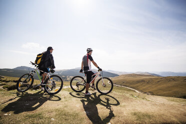 Friends standing with bicycles on mountain against sky - CAVF17836