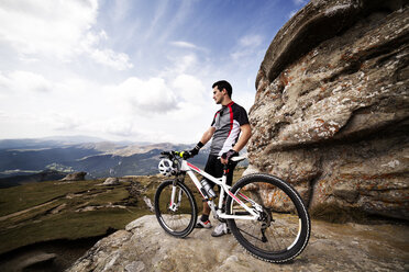 Männlicher Sportler mit Fahrrad auf einem Berg stehend gegen den Himmel - CAVF17837