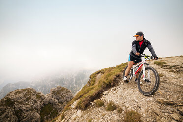 Männlicher Sportler mit Fahrrad auf einem Berg gegen den Himmel - CAVF17839
