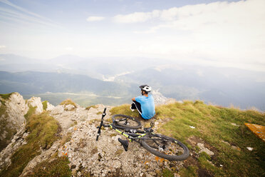 Rear view of man sitting by bicycle on mountain against sky - CAVF17842