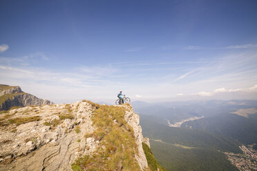 Entfernte Ansicht von Mountainbiker mit Fahrrad auf Klippe gegen Himmel stehend - CAVF17845