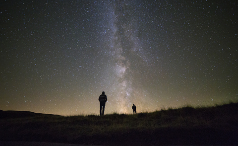 Freunde stehen vor einem nächtlichen Sternenfeld, lizenzfreies Stockfoto