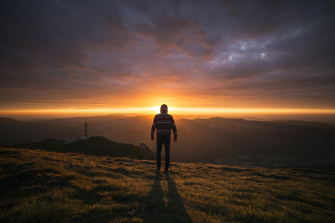 Rückansicht eines auf einem Berg stehenden Mannes bei Sonnenuntergang, lizenzfreies Stockfoto