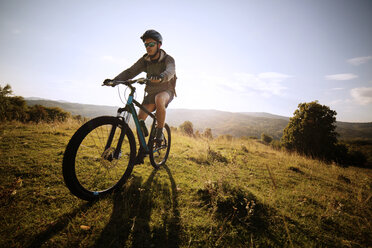 Male athlete cycling on field against sky - CAVF17868