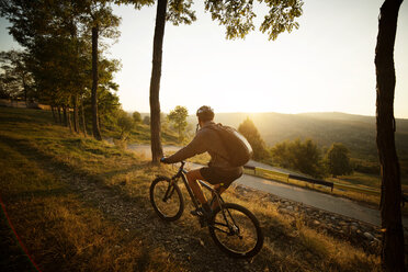 Male athlete cycling on footpath in field against clear sky - CAVF17871