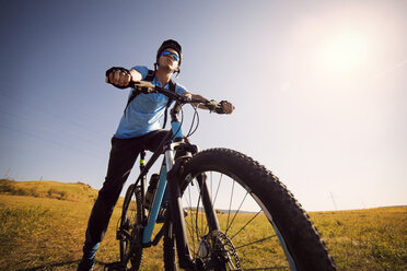 Low angle view of male athlete on bicycle in field against clear sky - CAVF17874