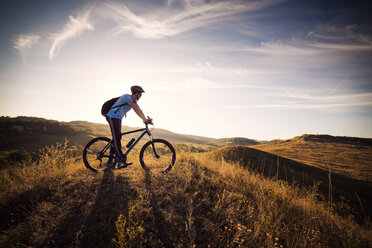 Männlicher Sportler auf einem Fahrrad auf einer Wiese vor bewölktem Himmel - CAVF17876