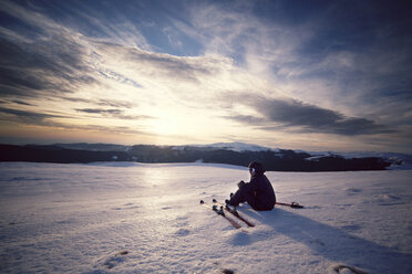 Skifahrer, der die Aussicht betrachtet, während er auf einem schneebedeckten Berg gegen den Himmel sitzt - CAVF17922