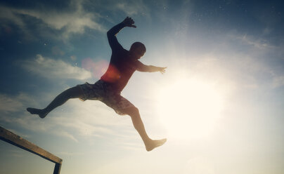 Low angle view of excited man in mid-air against sky on sunny day - CAVF17975