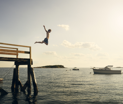 Hemdloser Mann taucht von der Seebrücke ins Meer gegen den Himmel, lizenzfreies Stockfoto