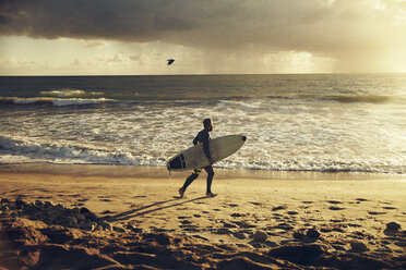 Mann mit Surfbrett beim Strandspaziergang bei Sonnenuntergang - CAVF18084