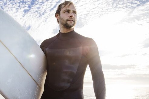 Mann, der ein Surfbrett trägt, während er vor einem bewölkten Himmel steht - CAVF18090