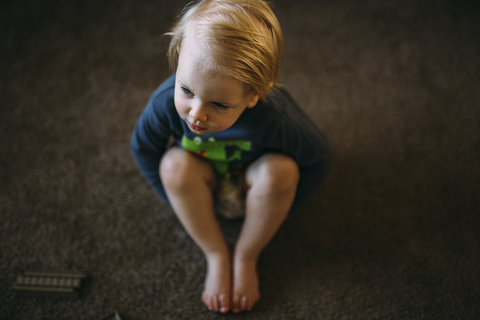 Hoher Blickwinkel auf einen Jungen, der zu Hause auf dem Boden sitzt, lizenzfreies Stockfoto