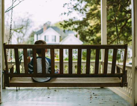 Rückansicht eines Jungen, der auf einer Schaukel auf der Veranda sitzt, lizenzfreies Stockfoto