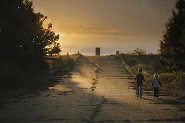 Rückansicht von Jungen, die auf der Straße gegen den Himmel bei Sonnenuntergang laufen - CAVF18144