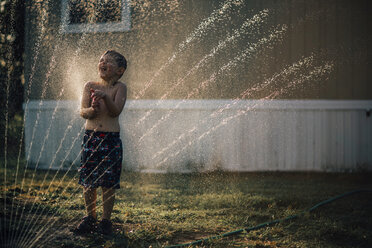 Junge genießt Wasser aus dem Sprinkler, während er im Garten steht - CAVF18148